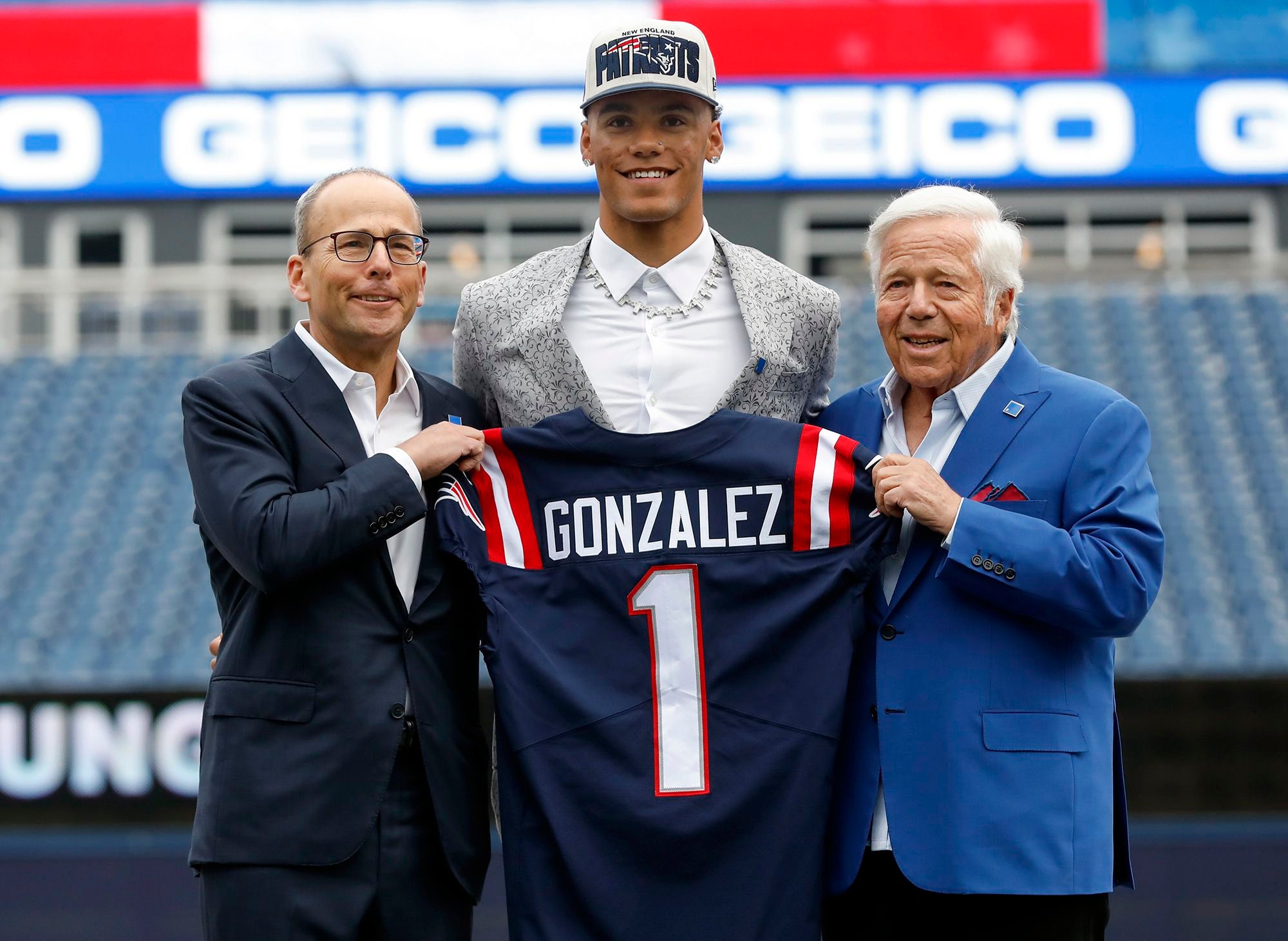 Christian Gonzalez holding up a Patriots jersey next to the Krafts.