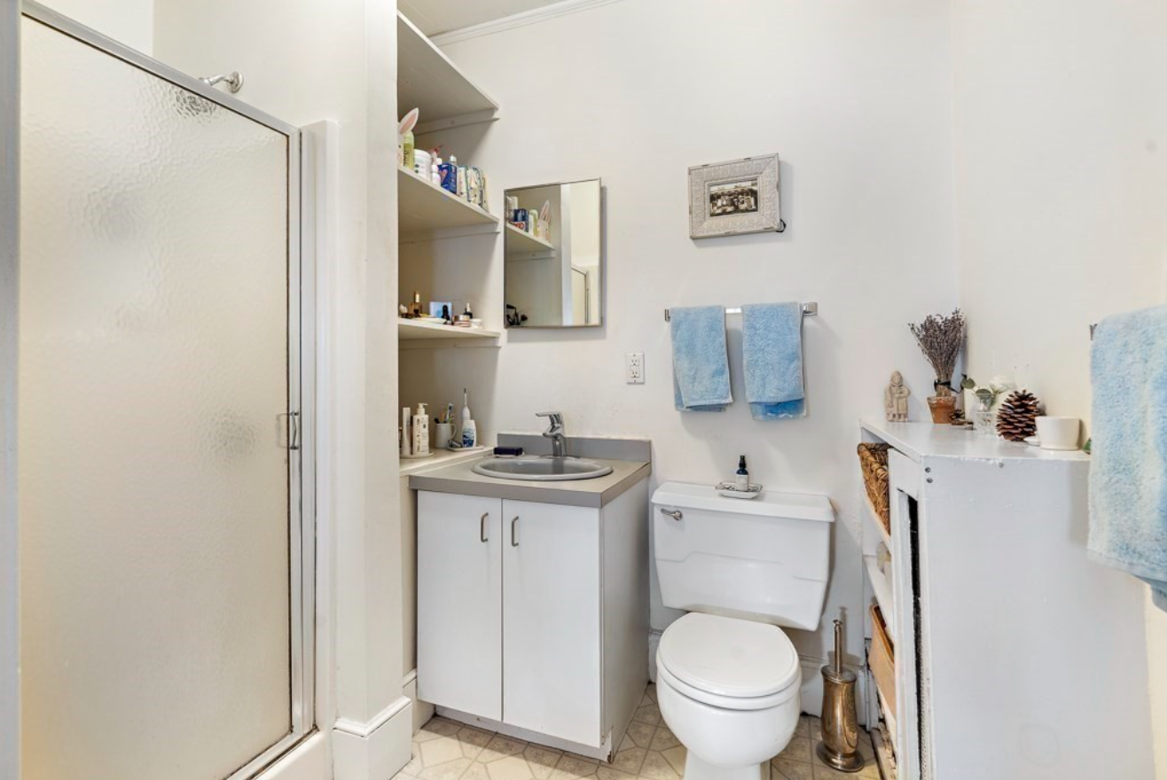 The bathroom includes built-in shelving and a semi-frameless shower, along with a single vanity.