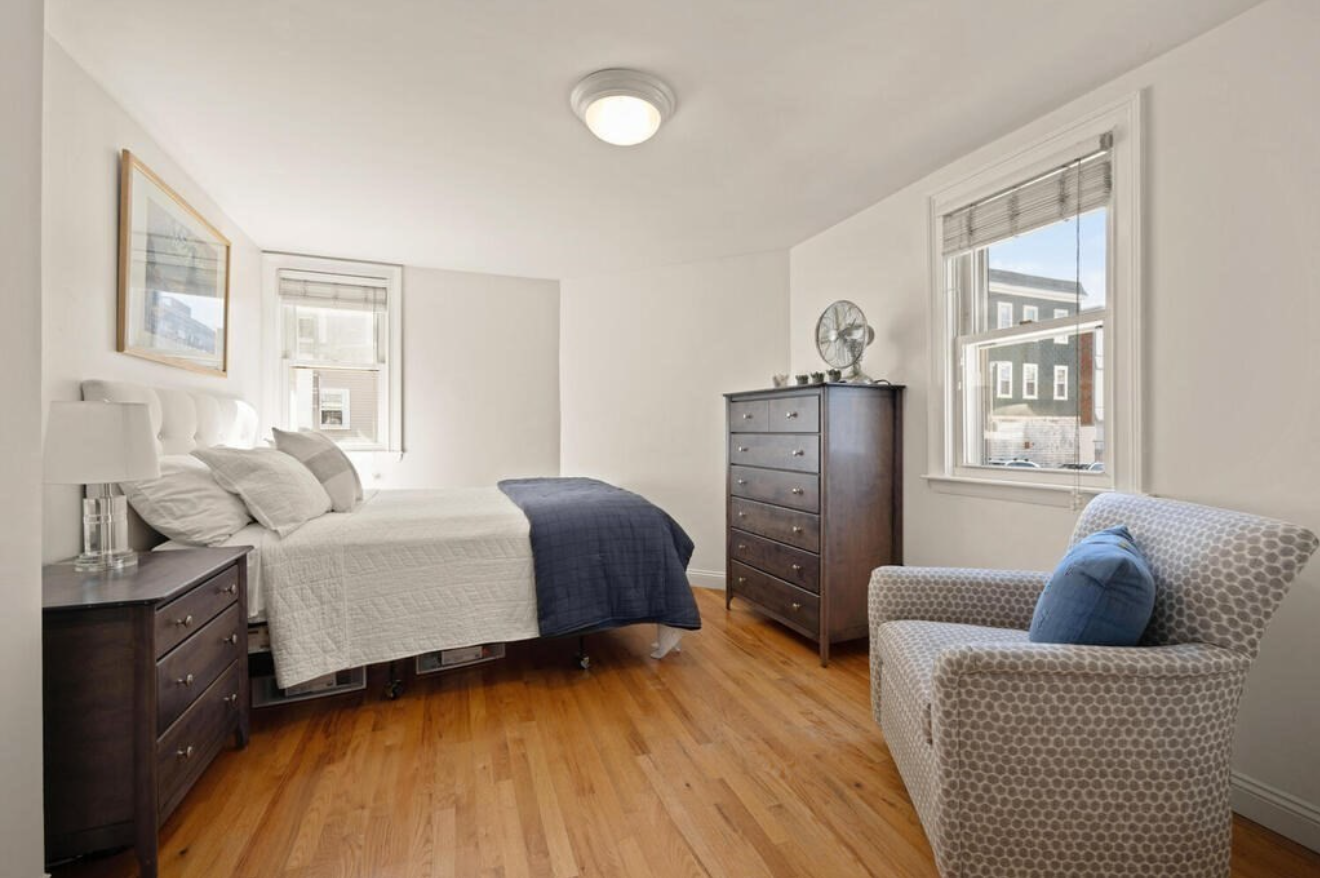 The primary bedroom has two single-hung windows, hardwood floors, and white walls.