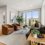 A living room with hardwood floors, light grey walls, and floor-to-ceiling windows.
