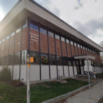 A rectangular brick building surrounded by grassy lawn and sidewalk, with a sign reading "Easthampton Municipal Building" on the front-facing facade.