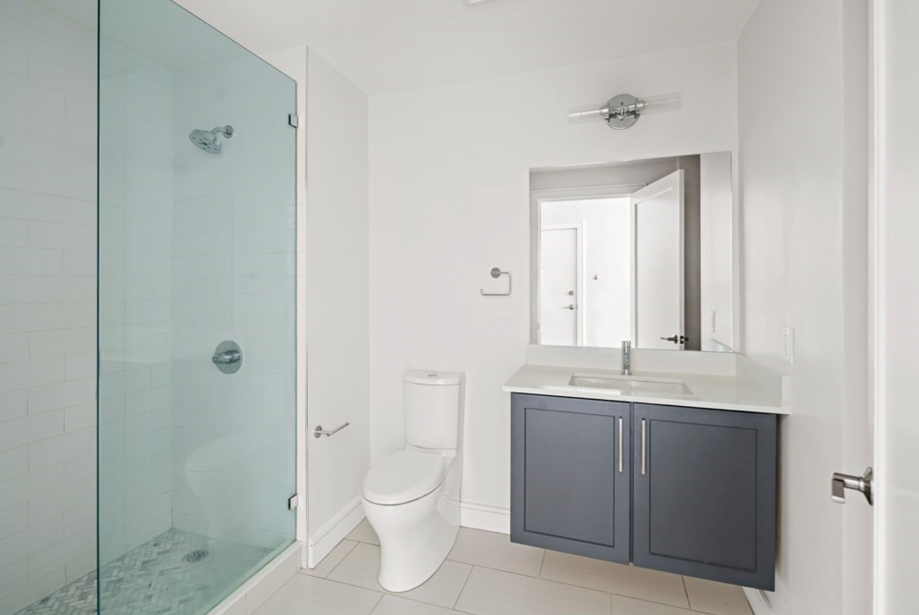 The bathroom has a semi-frameless shower and single vanity with dark blue-grey cabinetry.