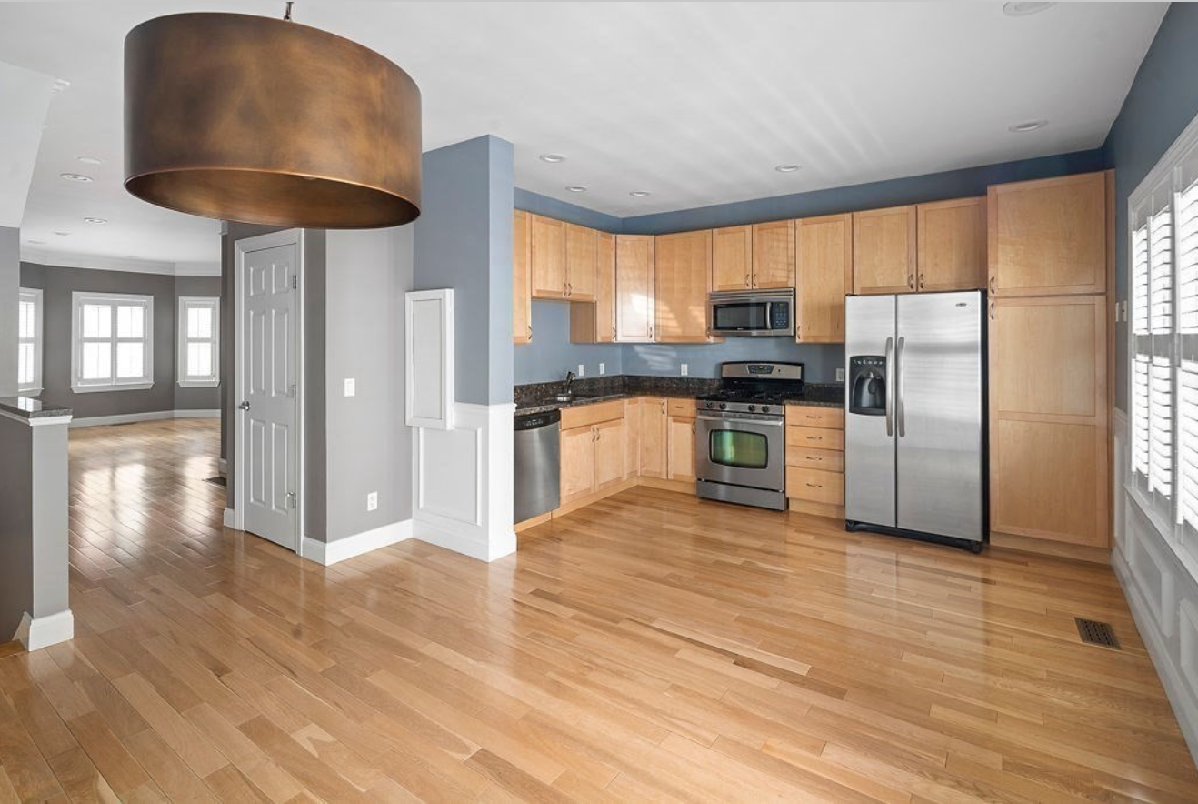 The kitchen has wooden cabinets and hardwood floors, stainless steel appliances, and light blue-grey walls.