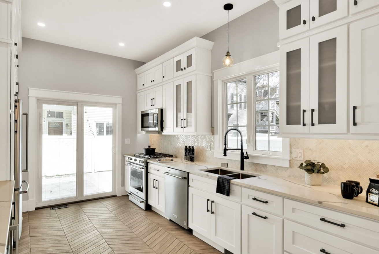 Kitchen with white Shaker-style cabinets, herringbone tile floors, light grey walls, and pendant lighting.