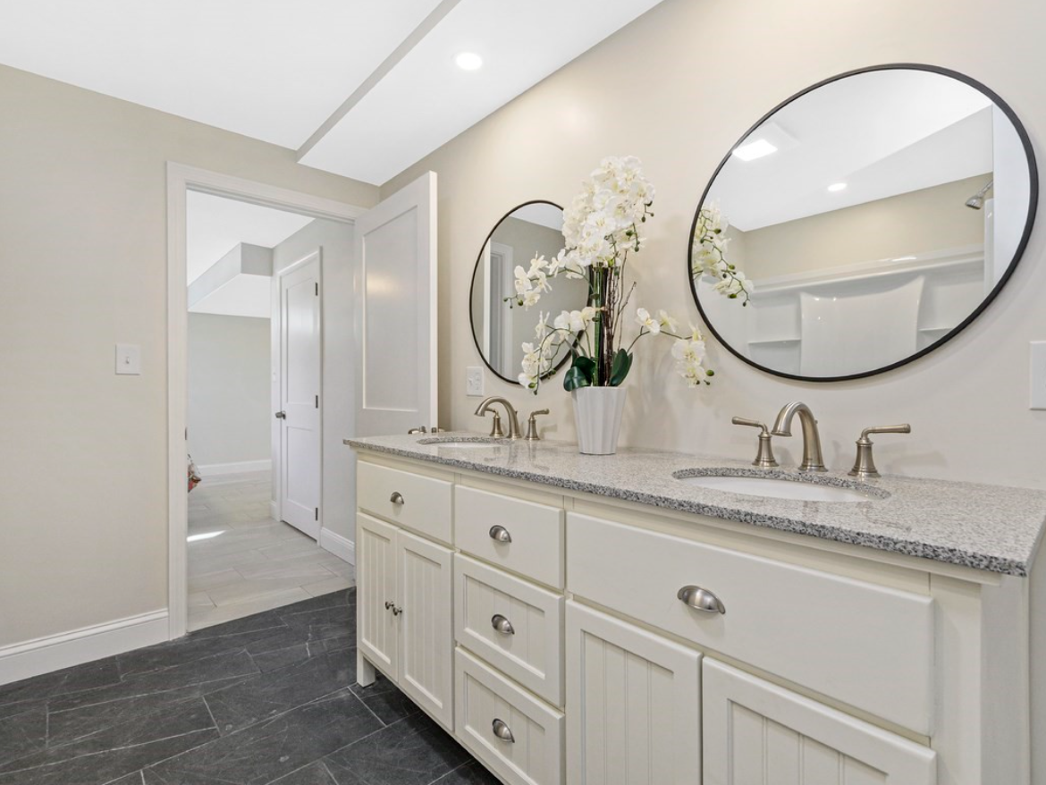 Bathroom with double vanity, circular mirrors, and white cabinetry.