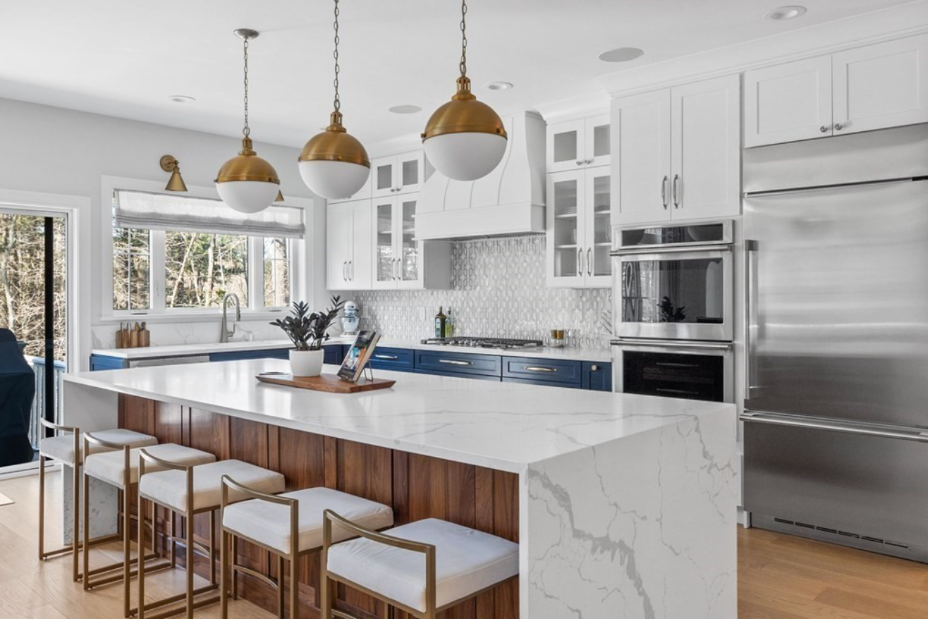 Kitchen with white flat panel cabinets, stainless steel appliances, and pendant lighting above an island with seating for four.