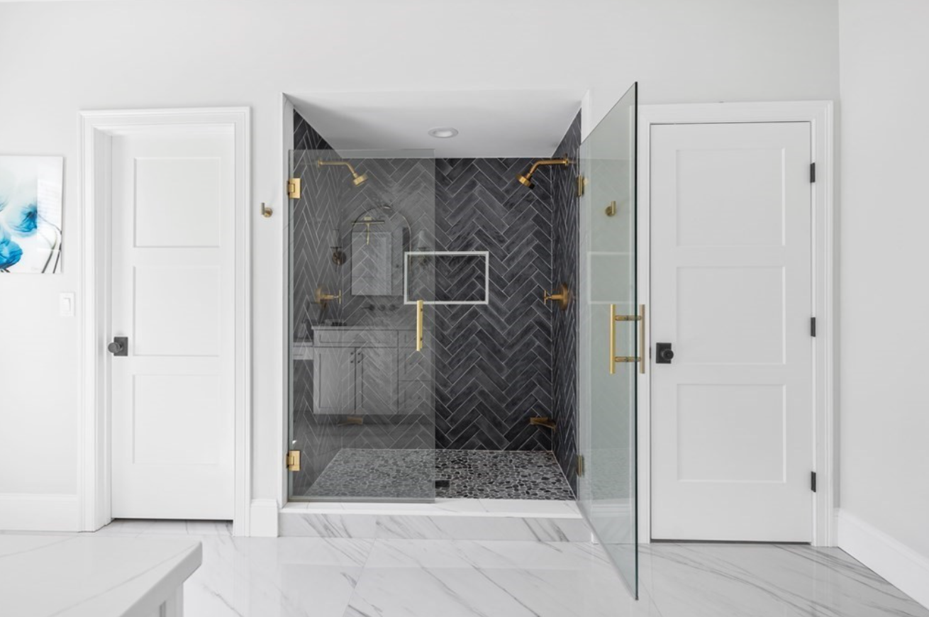 Semi-frameless shower with black herringbone tiling and gold hardware