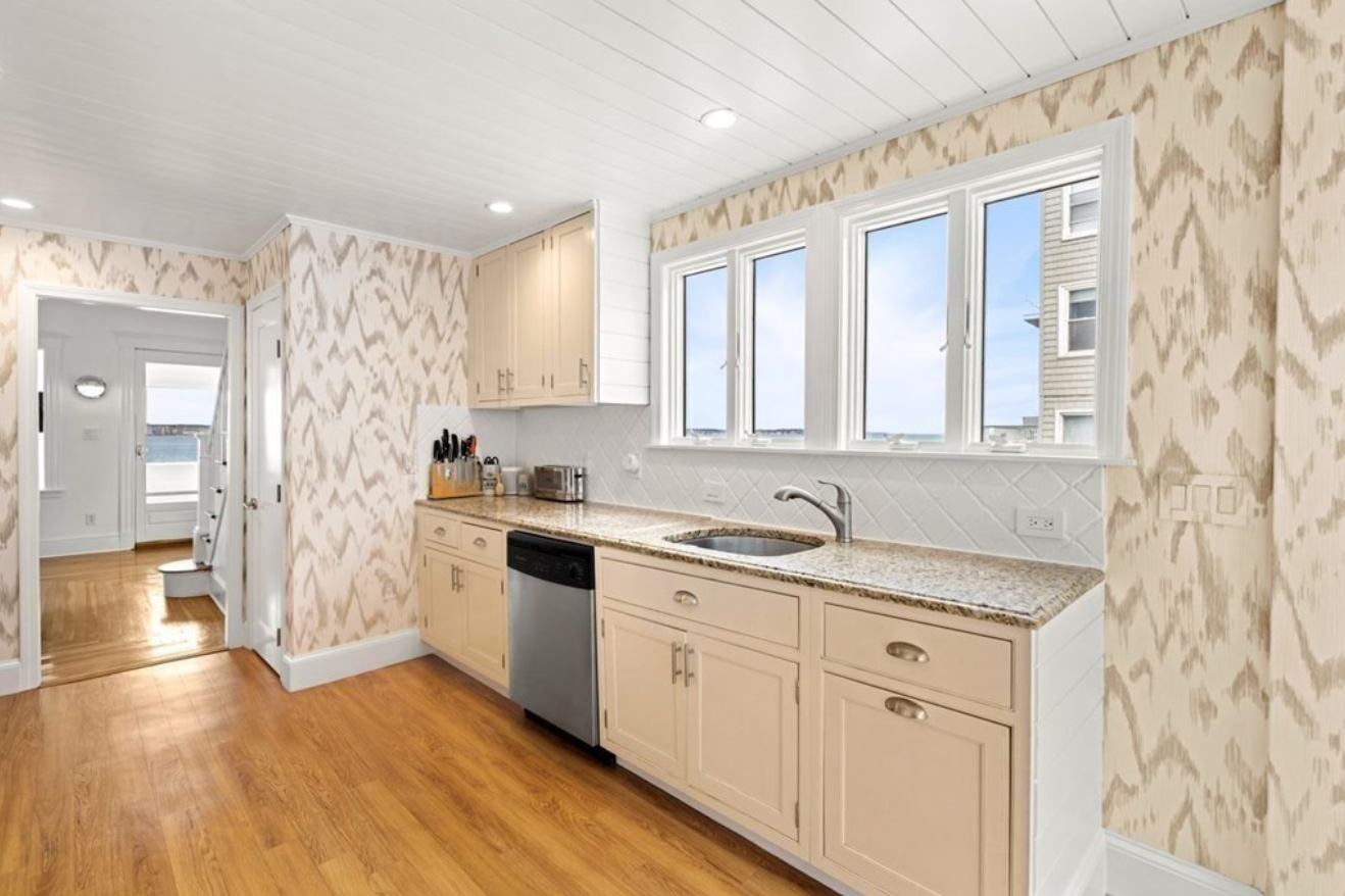 Kitchen with cream cabinetry and stainless steel appliances. The wallpaper has an abstract beige and cream design.