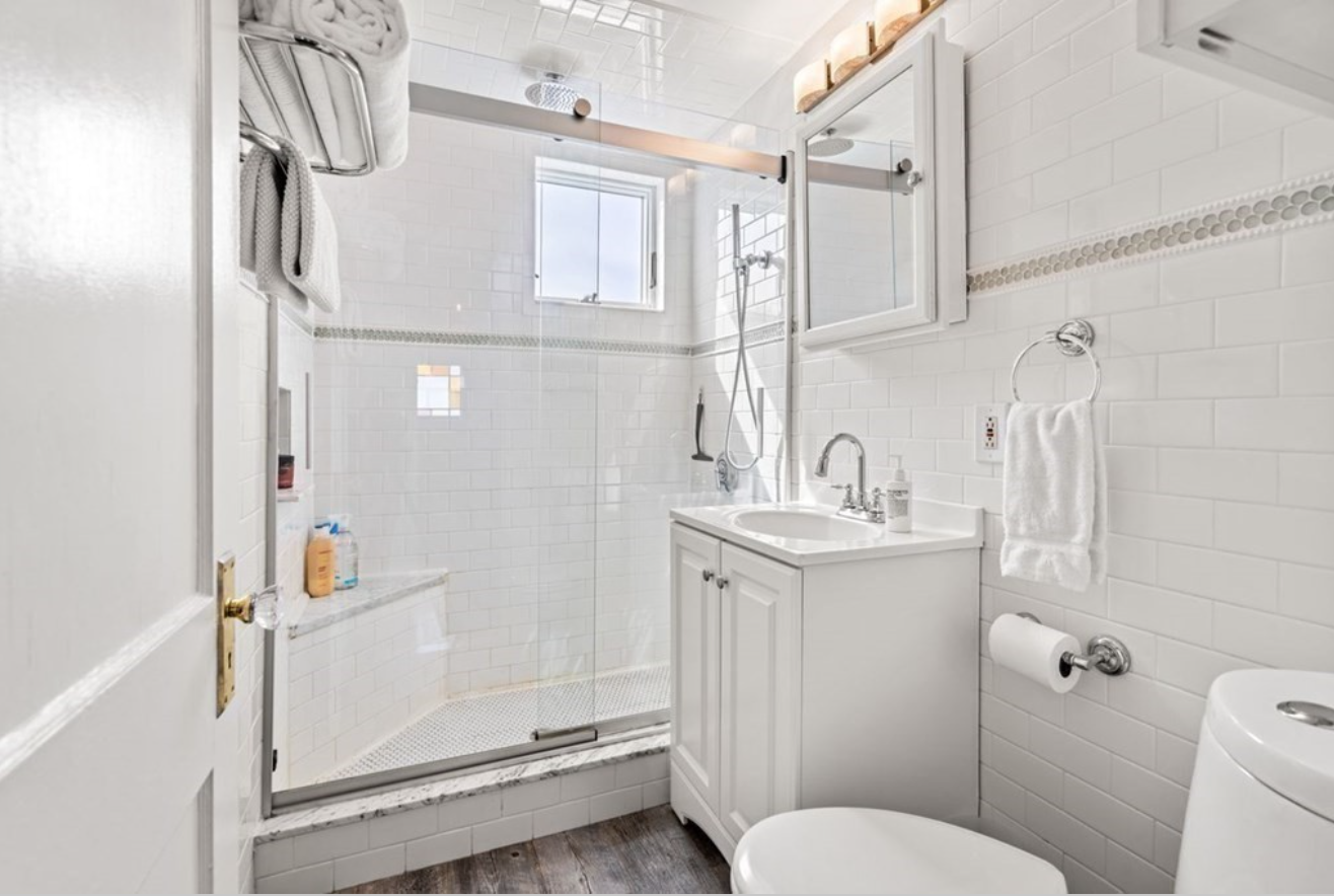 Another full bathroom includes a single vanity with white cabinetry, a semi-frameless shower, and all-white tiling.