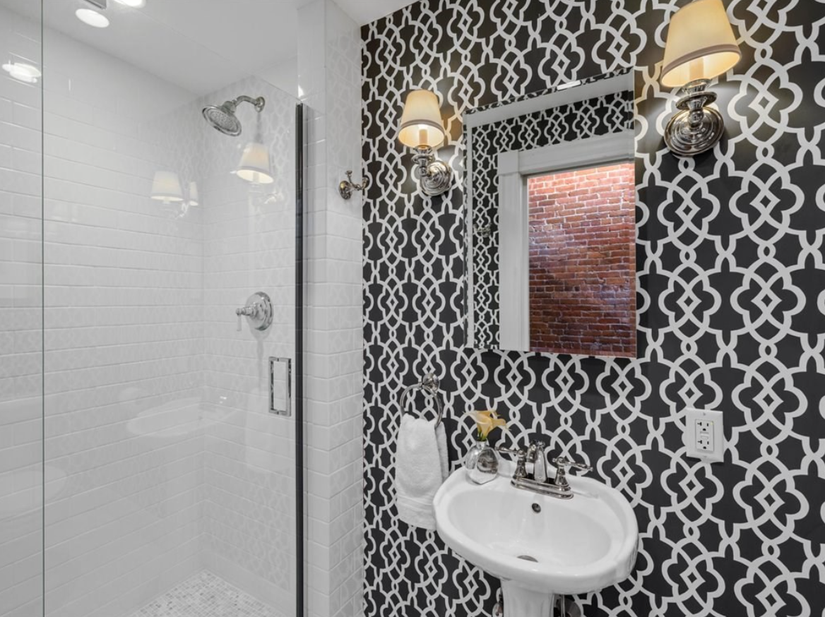 Bathroom with black and white patterned wallpaper, a single vanity, and semi-frameless shower.