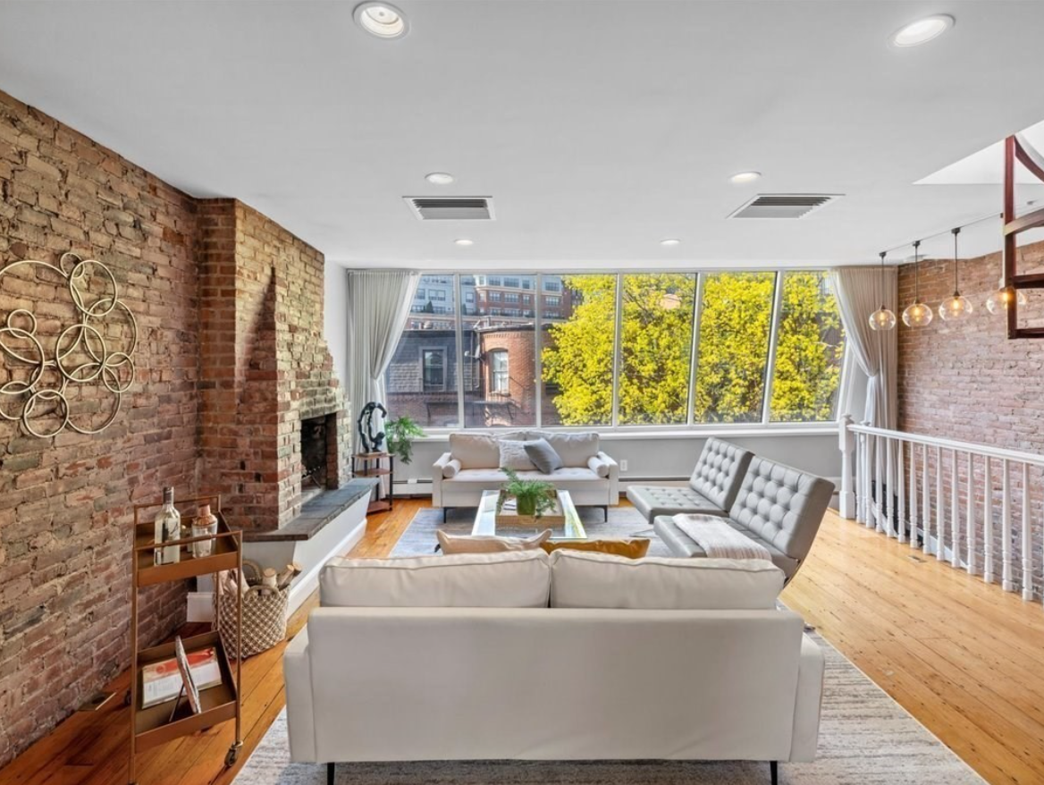 The living room has exposed brick walls, floor to ceiling windows, and hardwood floors.