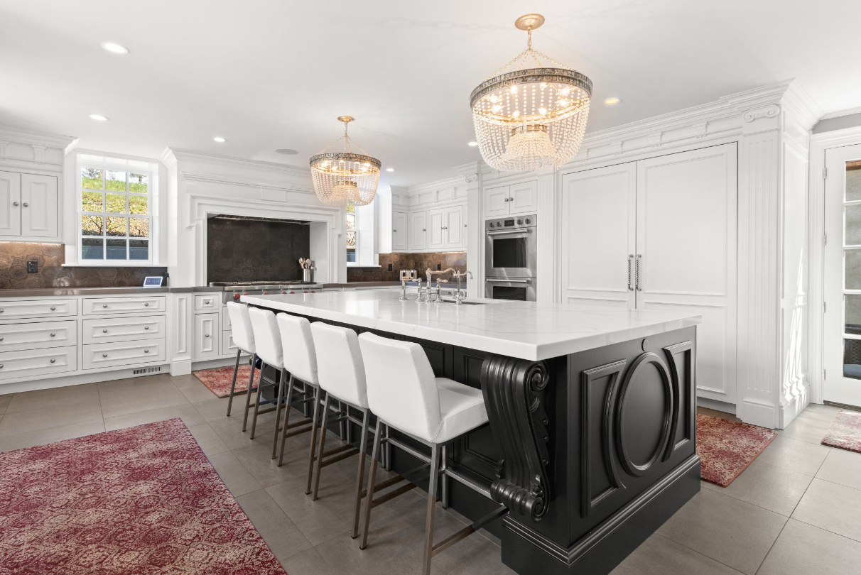 Kitchen with fully-functional island, white recessed-panel cabinetry, stainless steel appliances, and identical beaded chandeliers.