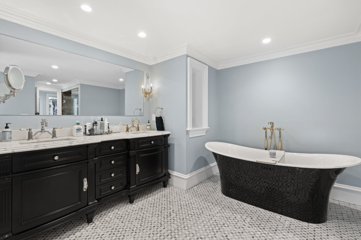 Bathroom with black soaking tub, double vanity with black cabinetry, and light blue walls.