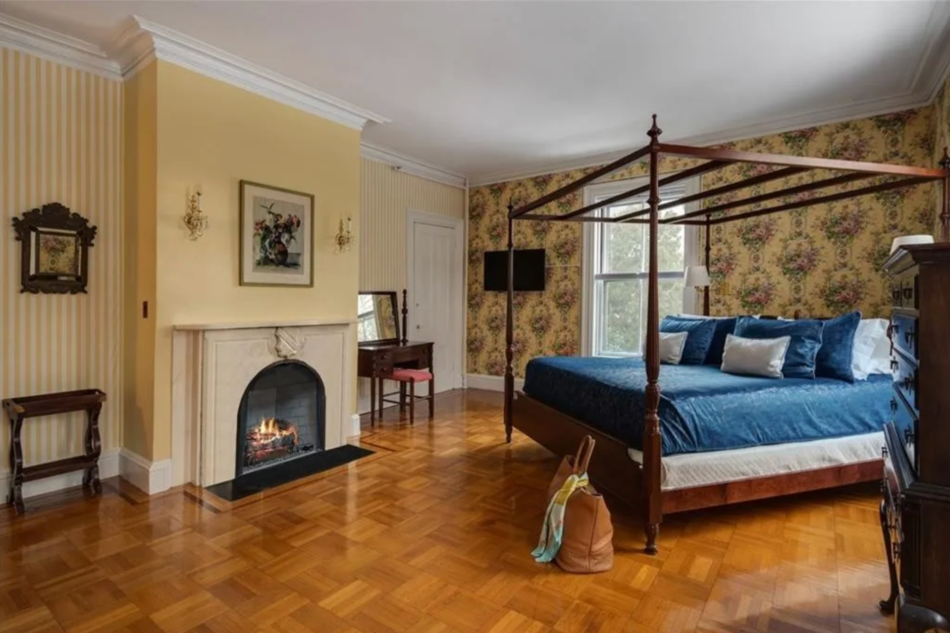 This bedroom has light yellow walls and a yellow patterned accent wall, a gas fireplace, and hardwood floors.