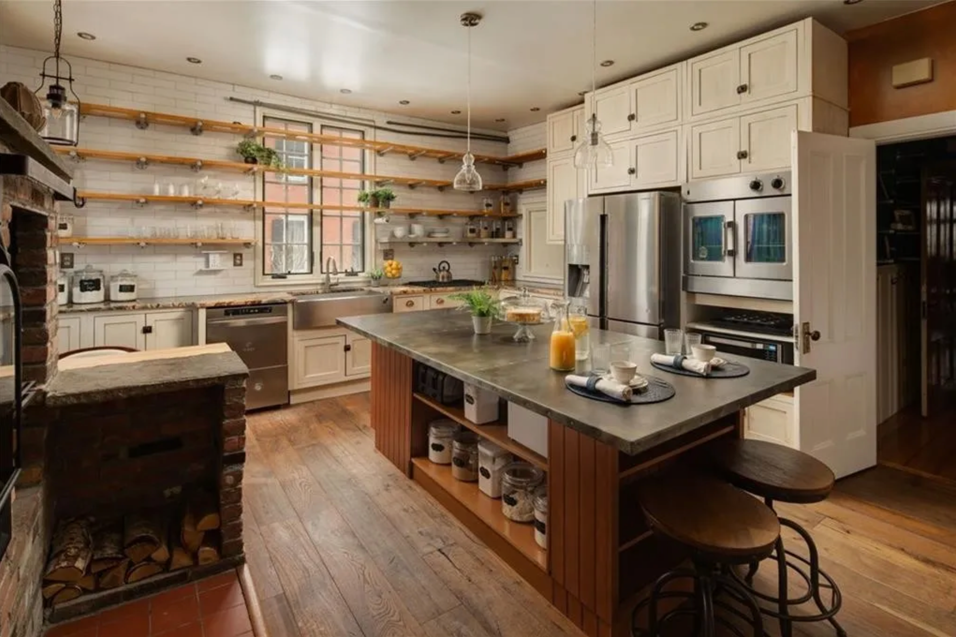 The kitchen has hardwood floors and stainless steel appliances, as well as cream shaker-style cabinets and exposed wooden floating shelves.