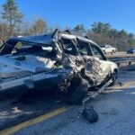 A damaged Subaru rests on the side of the road after being struck by a van