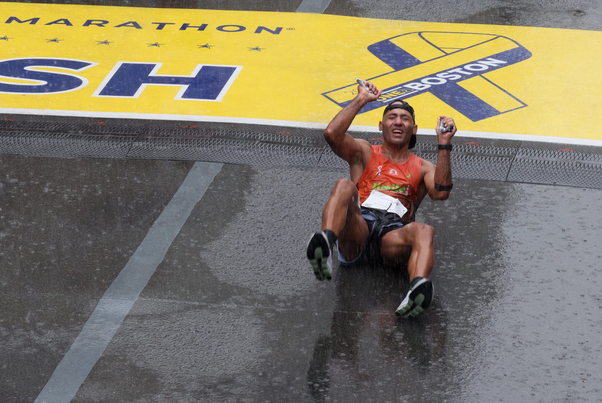 A runner somersaults across the Finish Line as rain falls at the Boston Marathon.