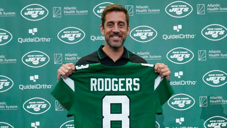 Aaron Rodgers holding up his new Jets jersey with the number 8 on it.