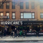 Diners are shown seated outside at tables set up on the sidewalk in front of Hurricane's on Canal Street. There is enough room on the sidewalk for pedestrians to pass by.