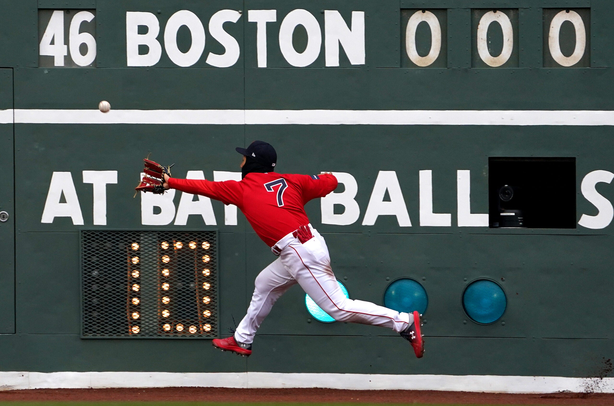 Masataka Yoshida unsuccessfully reaches for a fly ball in front of the Green Monster scoreboard.