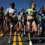 Elite runners Des Linden, left, and Molly Seidel stretch out before the start of the 2022 Boston Marathon.