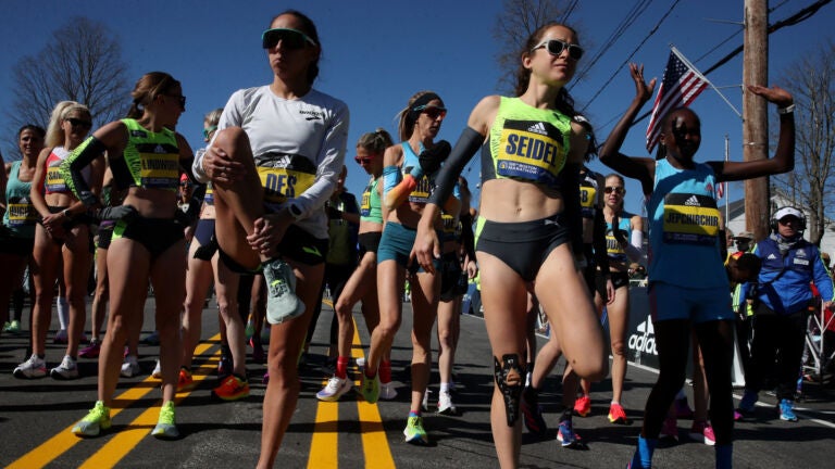 Elite runners Des Linden, left, and Molly Seidel stretch out before the start of the 2022 Boston Marathon.