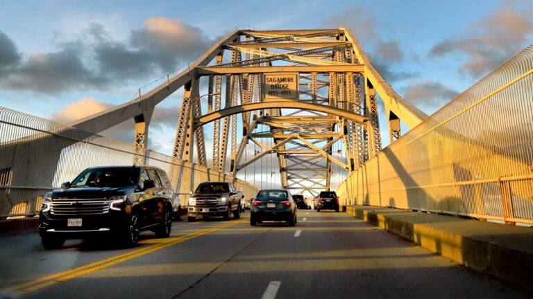 The sun reflects off the Sagamore Bridge as several cars drive across it.