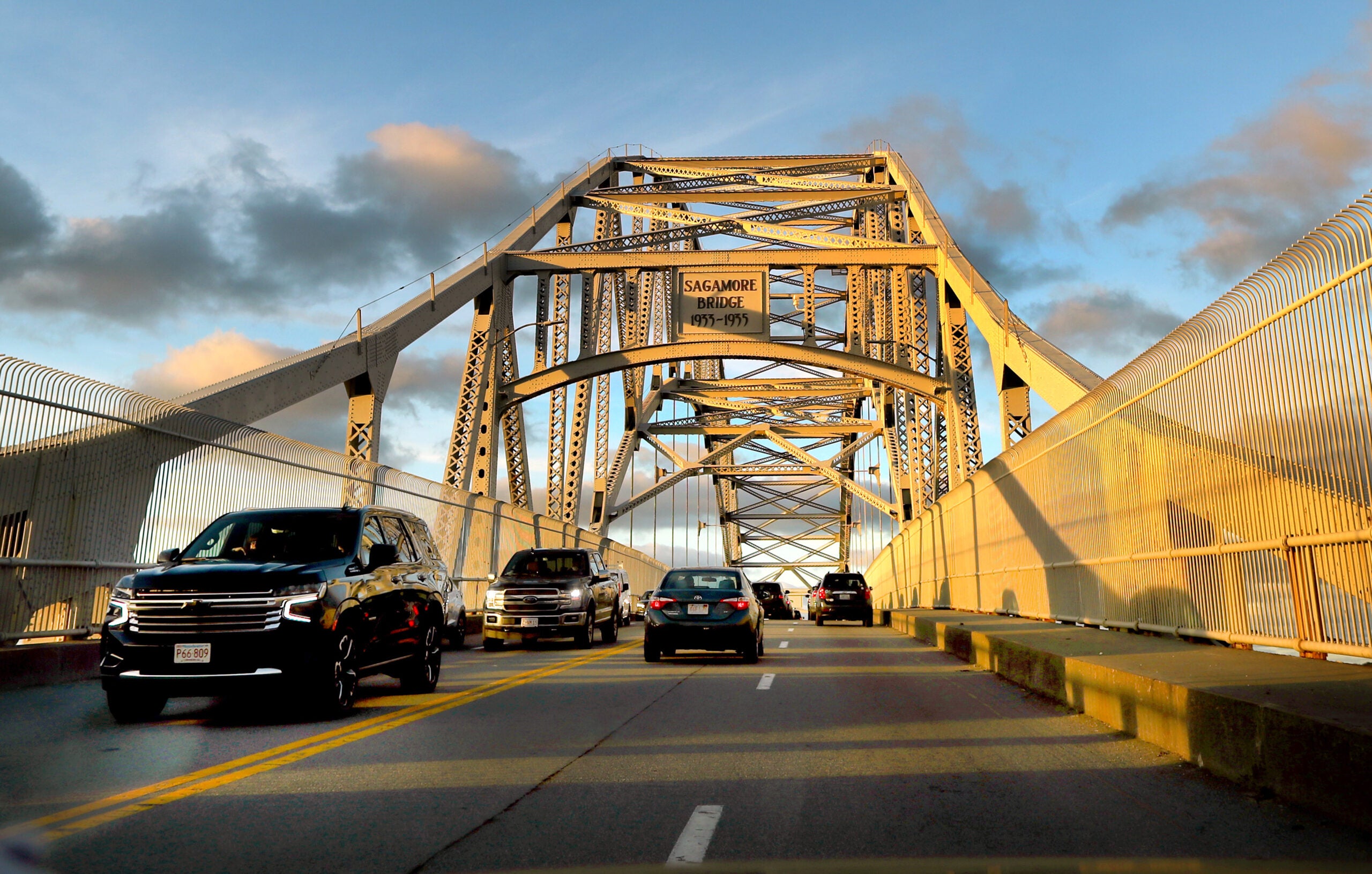 The sun reflects off the Sagamore Bridge as several cars drive across it.