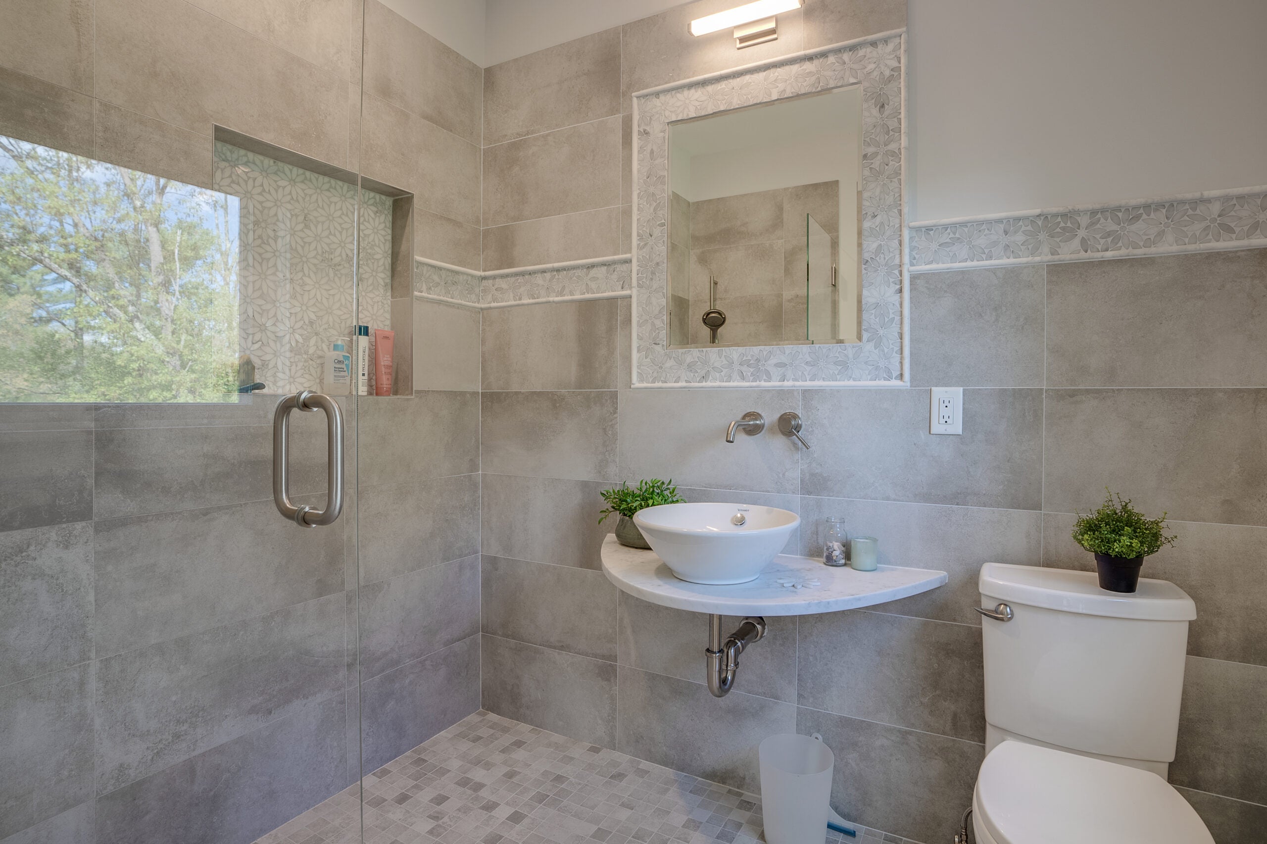 A bathroom with a glass-enclosed shower and a wall-mounted stone sink.