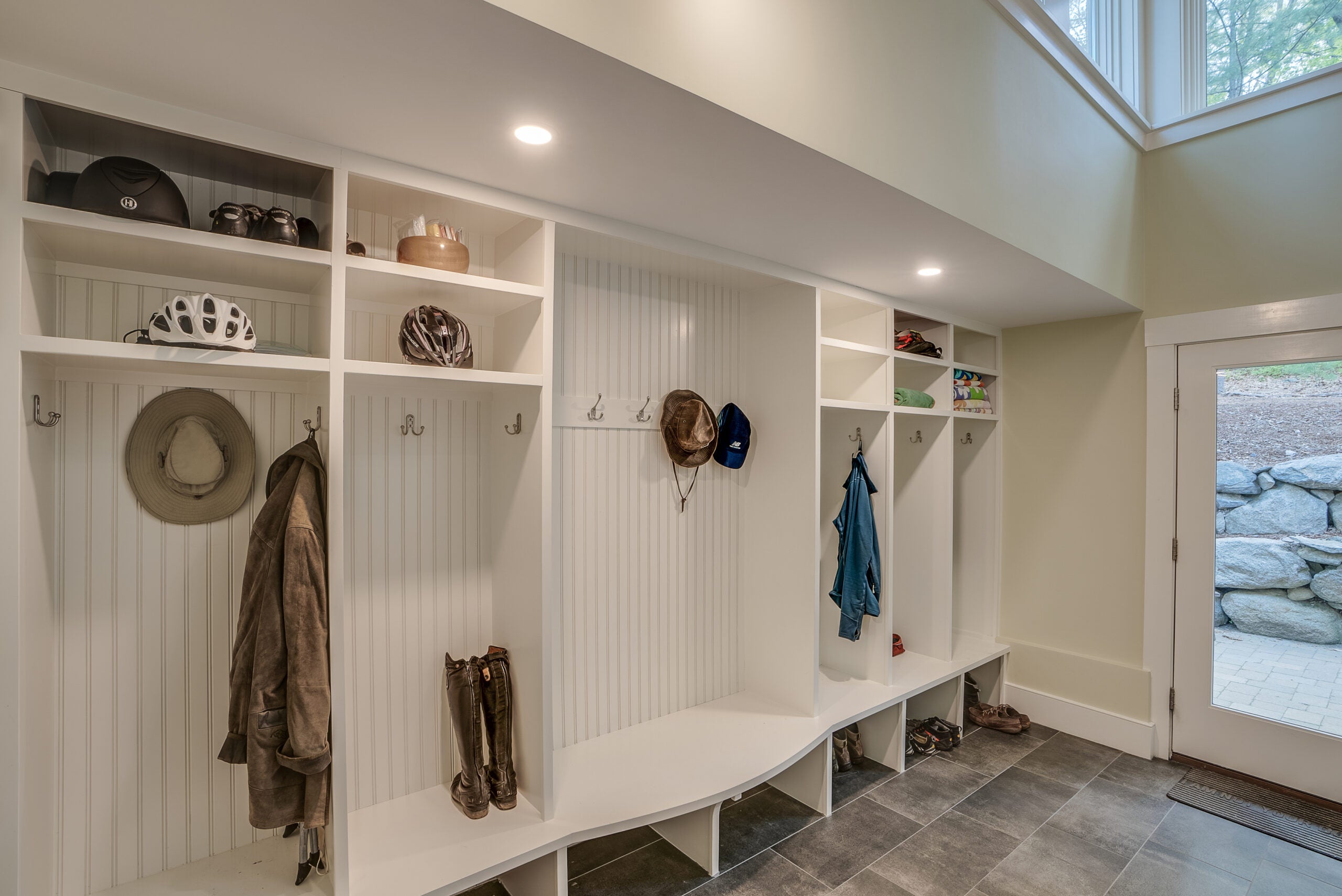 A mudroom with a tile floor, recessed lighting, and white bead-board cubbies with benches and shelving.