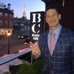 John Cena, wearing a blue plaid jacket, blue dress shirt, and pink tie with blue accents, poses at the Black Cow in Newburyport, Massachusetts.