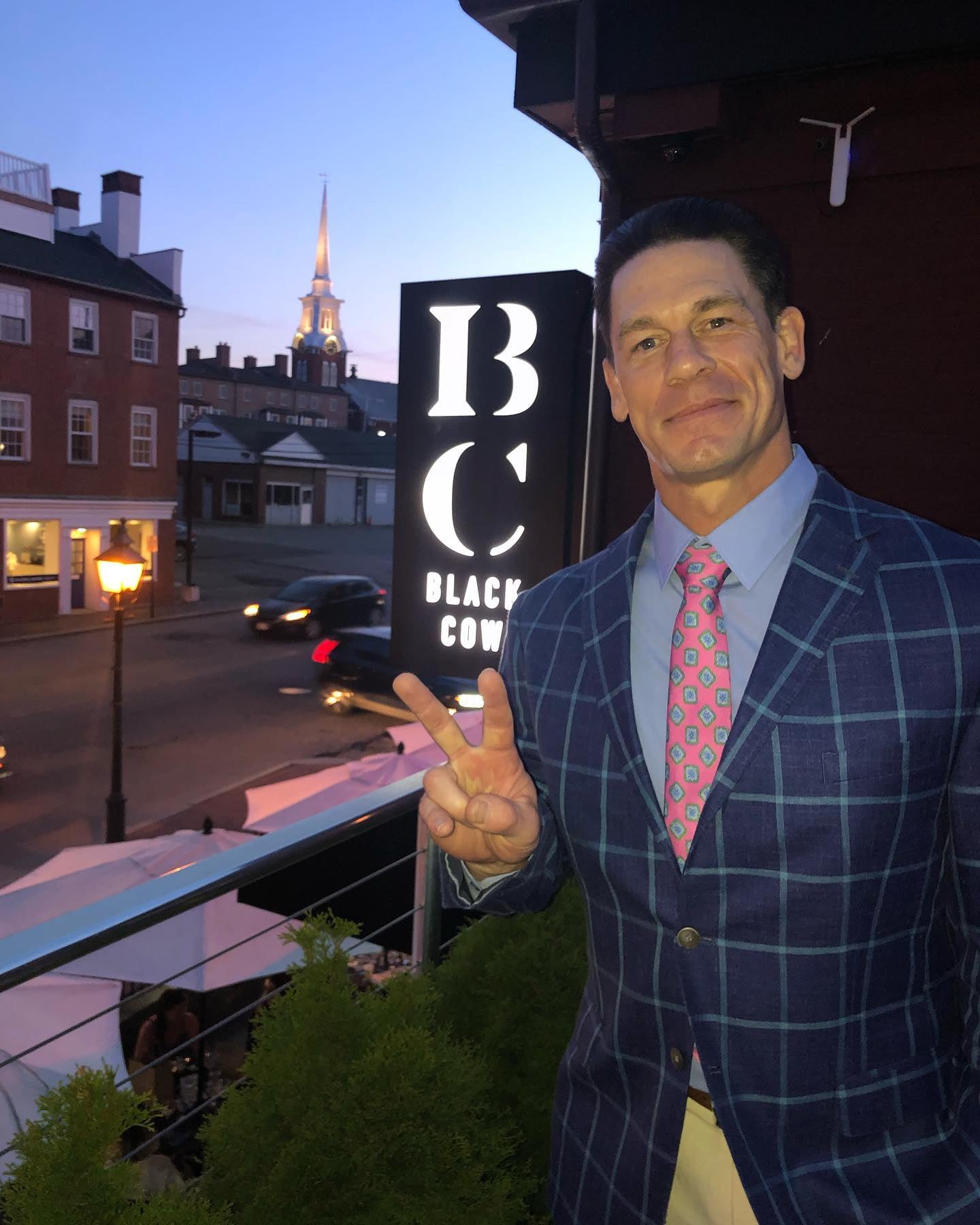 John Cena, wearing a blue plaid jacket, blue dress shirt, and pink tie with blue accents, poses at the Black Cow in Newburyport, Massachusetts.