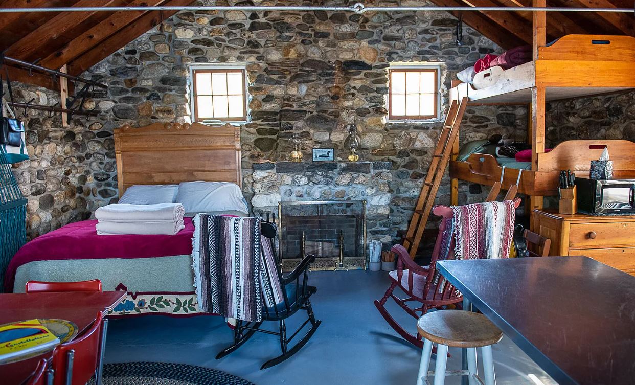 A bedroom area of a stone cottage with a full bed and a set of bunk beds on a Maine island with a lighthouse.