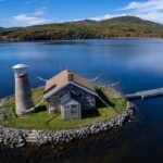 An aerial view of an island with a lighthouse and a stone cottage.