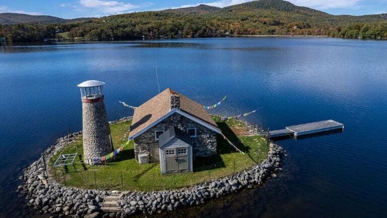 An aerial view of an island with a lighthouse and a stone cottage.