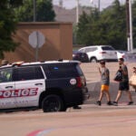 People raise their hands as they leave a shopping center following reports of a shooting, Saturday, May 6, 2023, in Allen, Texas.