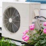 Air conditioning/ Heat pump unit on the side of a home among the flowers.