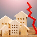 Real estate houses and a red arrow down to show a drop in home sales in this housing market.