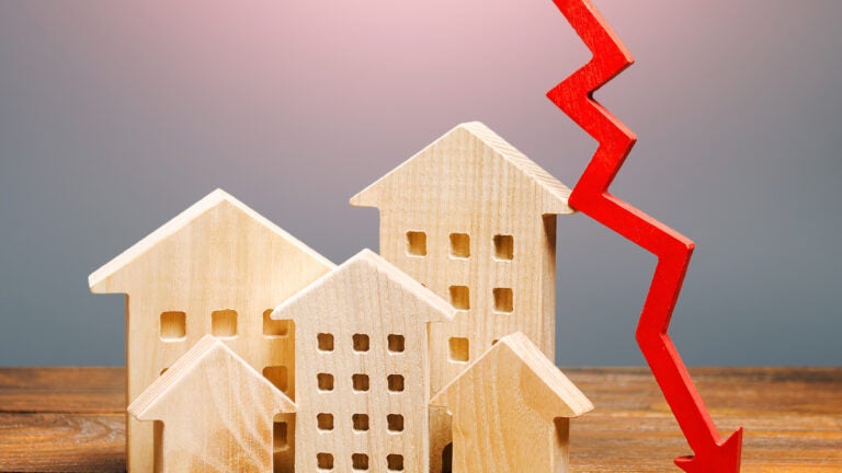 Real estate houses and a red arrow down to show a drop in home sales in this housing market.