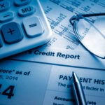 credit report on the desk to illustrate a credit rating. a calculator and a pair of glasses sit atop the paperwork.