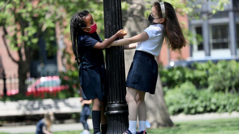 Boston weather , MA - 5/19/2021: Kindergartners from the Park Street School, Michaela Afework, left, and Tesla Long, played on a lamp post in the warm spring weather.