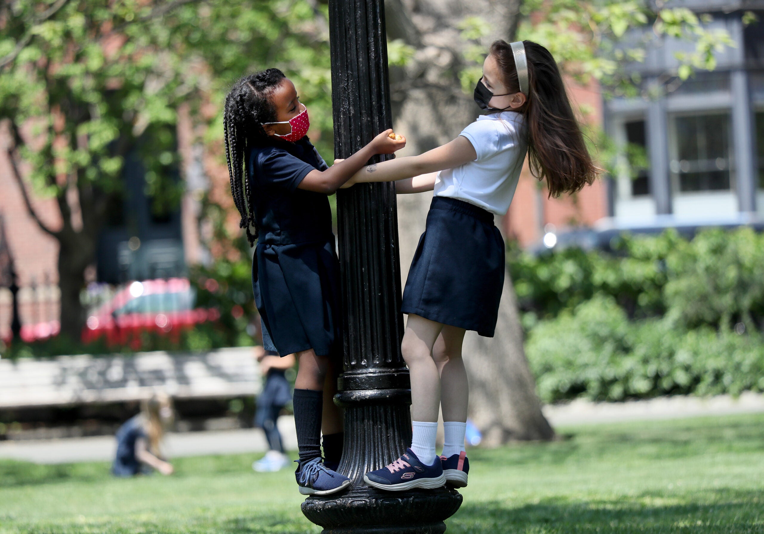 Boston weather , MA - 5/19/2021: Kindergartners from the Park Street School, Michaela Afework, left, and Tesla Long, played on a lamp post in the warm spring weather.