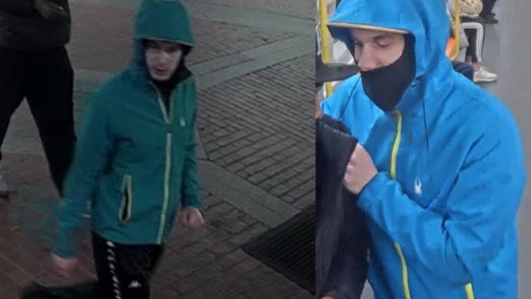 A man in a blue windbreaker and a black mask stands on an MBTA train