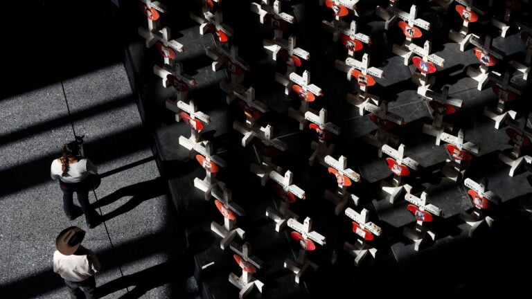alt = People look at a display of wooden crosses and a Star of David on display at the Clark County Government Center in Las Vegas in 2018.
