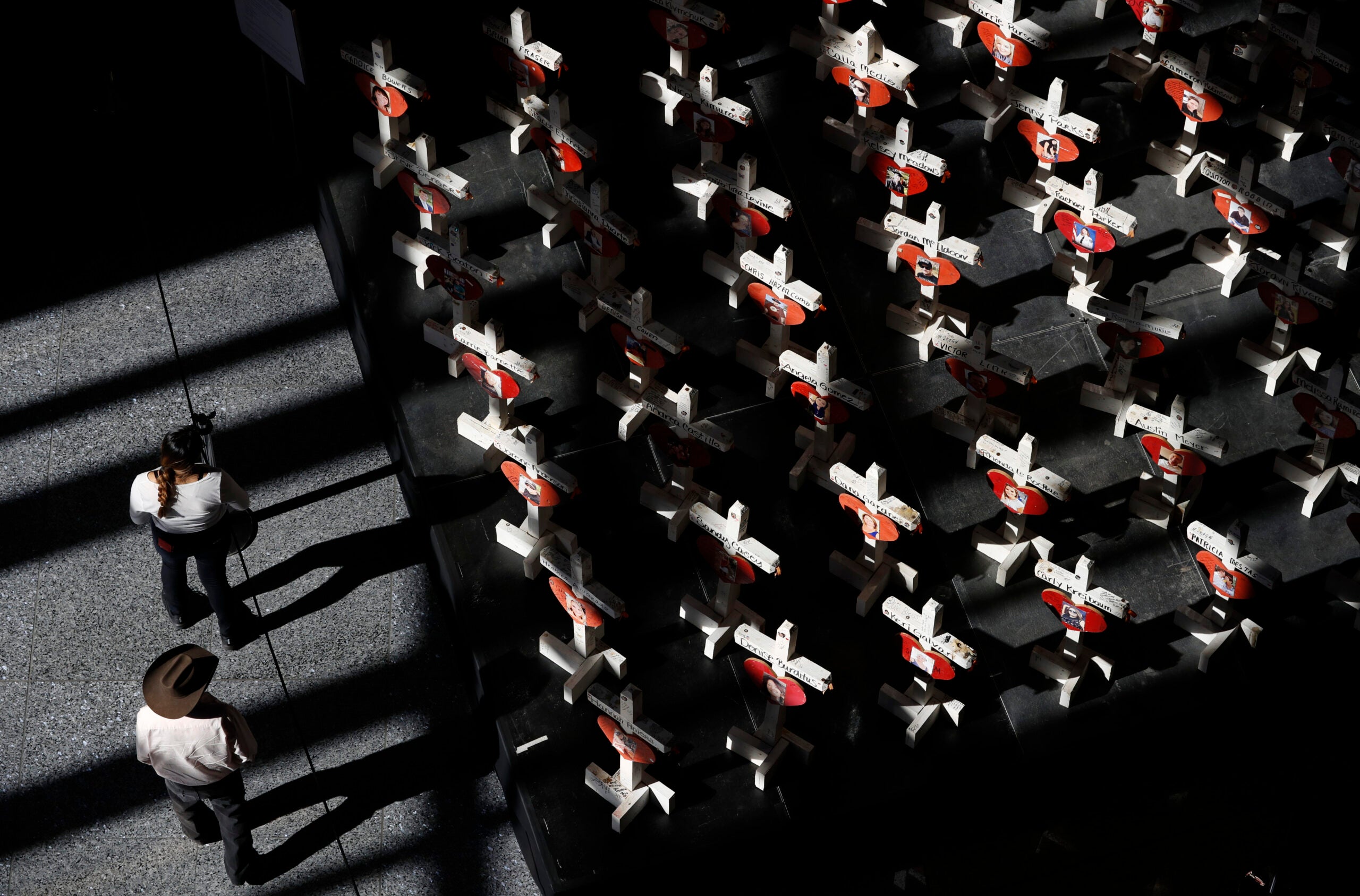 alt = People look at a display of wooden crosses and a Star of David on display at the Clark County Government Center in Las Vegas in 2018.