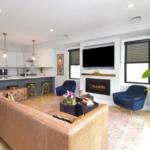 Jamaica Plain home ... Open-floor-plan living room and kitchen. The living room has single-hung windows and a gas fireplace. The kitchen has white cabinetry, stainless steel appliances, and pendant lighting.