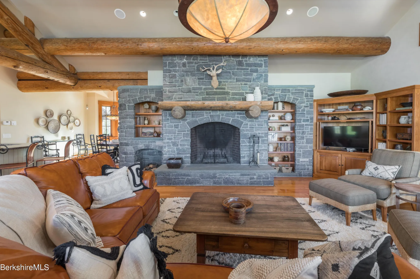 Living room with stone-clad fireplace, hardwood floors and vaulted ceilings with exposed wood beams.