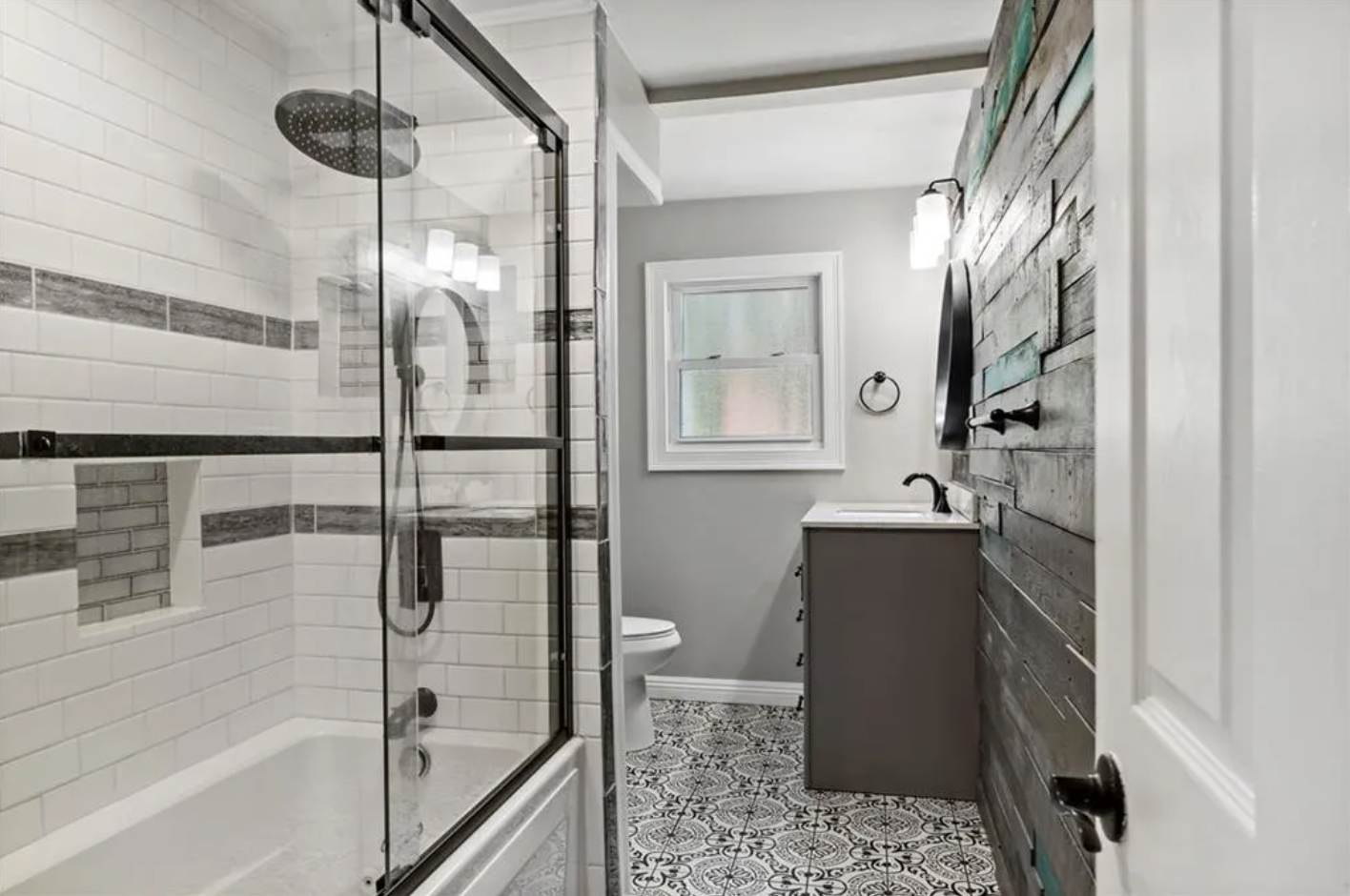 Bathroom with combination shower-bathtub, light gray walls, wood paneled accent wall, and single vanity.