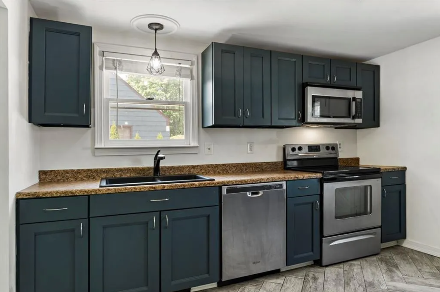 Kitchen with single-hung window, dark blue Shaker-style cabinets and stainless steel appliances.