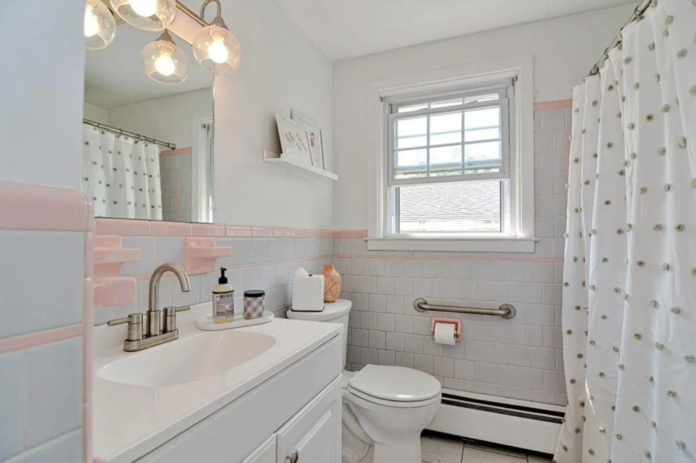 Bathroom with white walls, single vanity, and light gray and pink tiling. 